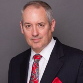 A man in a suit and tie standing up against a gray background.