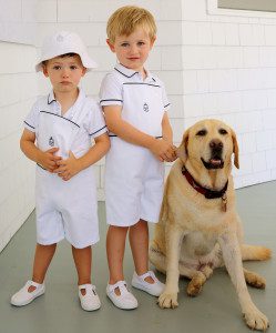 Two young boys in white outfits standing next to a dog.